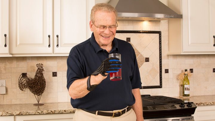 Older man wearing SaeboGlove holding glass